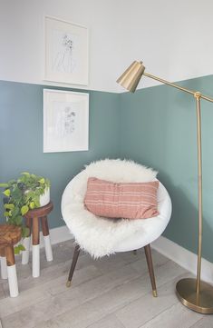 a white chair with a pink pillow on top of it next to a lamp and potted plant