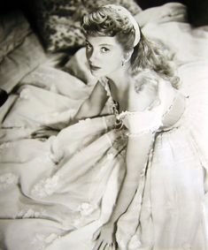 an old black and white photo of a woman in a dress laying on a bed