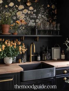 a black kitchen with flowers on the wall and gold faucets in the sink