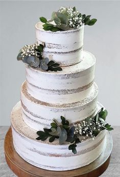 a three tiered white cake with greenery on the top and bottom, sitting on a wooden platter