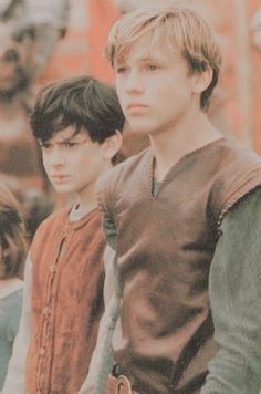 two young boys standing next to each other in front of a group of people wearing medieval clothing