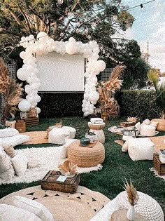 an outdoor movie party with white balloons and pillows on the grass in front of a large screen