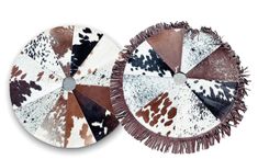 two brown and white cowhide plates with tassels on the sides, one is round