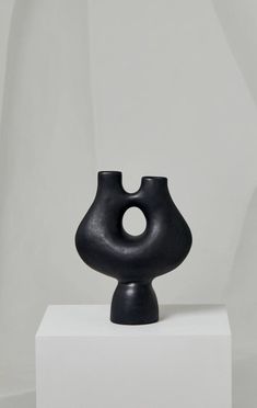 a black vase sitting on top of a white pedestal