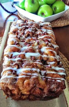 a loaf of cinnamon apple bread sitting on top of a table next to a bowl of green apples