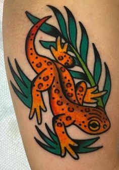 an orange and black gecko tattoo on the thigh with green leaves around its legs