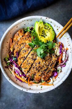 a white bowl filled with meat and veggies next to two chopsticks