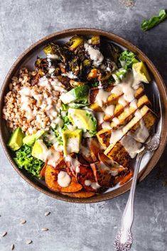 a bowl filled with meat, vegetables and rice on top of a gray surface next to a spoon