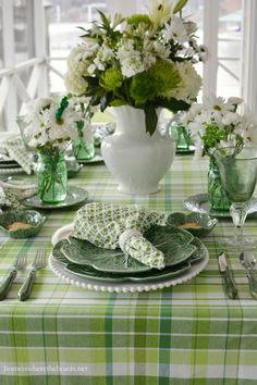 the table is set with green and white dishes, silverware, and flowers in vases