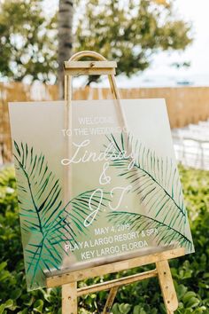 an easel with a sign that says welcome to the wedding and is decorated with palm leaves