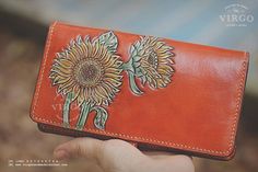 a hand holding an orange wallet with sunflowers on the front and back side