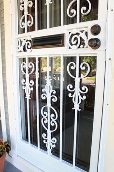 the front door is decorated with white wrought iron designs and glass panels, along with a potted plant