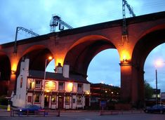 an old brick bridge over a street with cars parked on the side and people walking under it