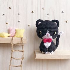 a crocheted cat sitting on top of a shelf next to a small doll