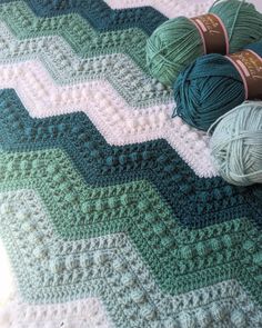 three balls of yarn sitting on top of a crocheted blanket next to each other