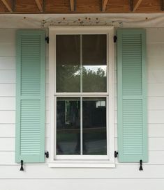 a white house with green shutters and a cat sitting on the window sill