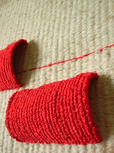 two red pieces of yarn sitting on top of a bed