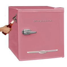 a hand holding a bottle opener over a pink refrigerator