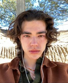 a young man with earphones on his ears looking at the camera while standing in front of a tree