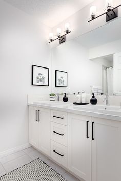 a white bathroom with black and white flooring, framed pictures on the wall and two sinks