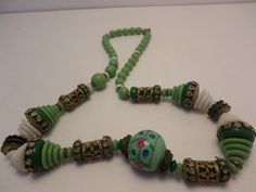 "Vintage 1930's Deco ethnic all glass multi shaped beads with brass details. Fabulous jadite green emerald green white middle bead has pink and blue flowers. 16\" brass details. fabulous looking necklace! condition is great, there is one knotted string coming through top of bead, not unusual with this type of thing." Vintage Adjustable Jade Necklace, Adjustable Vintage Jade Necklace, Adjustable Vintage Jade Necklaces, Vintage Adjustable Jade Necklaces, Vintage Jade Beaded Necklace, Vintage Jade Beaded Necklaces, Vintage Green Beads For Jewelry Making, Vintage Green Beaded Necklace With Round Beads, Vintage Large Green Beads