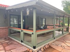 a screened in porch with seating and lights on the outside patio, surrounded by stone pavers