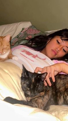 a woman laying in bed with two cats