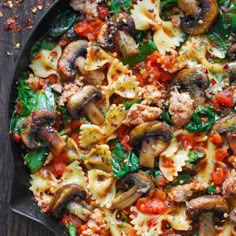 a skillet filled with pasta, mushrooms and spinach on top of a wooden table