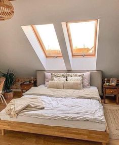 a bed sitting under two windows in a bedroom next to a wooden table and chair