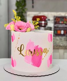 a white cake with pink flowers and gold lettering on it that says larousa