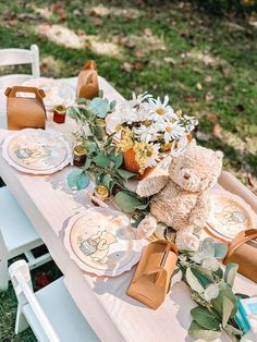 a teddy bear sitting on top of a table with plates and flowers in front of it