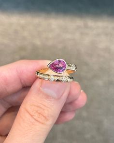 a person holding two rings with a pink stone in the middle and white diamonds around them