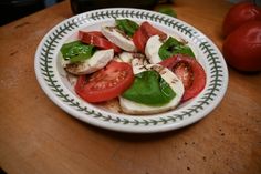 a white plate topped with sliced tomatoes and mozzarella on top of a wooden table