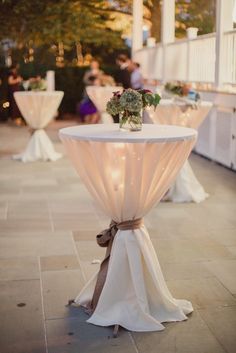 the table is set up with white linens and flowers on it for an outdoor wedding