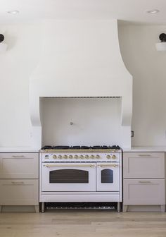 a white stove top oven sitting inside of a kitchen next to wooden floors and cabinets