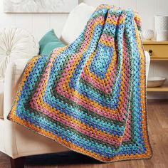 a crocheted blanket is sitting on a couch with a white chair in the background