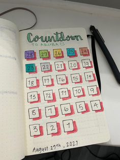 an open planner with colorful numbers on it and a black pen next to the calendar