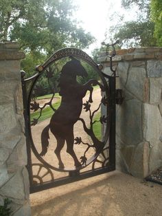 an iron gate with a horse on it in front of a stone wall and trees