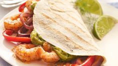 a taco filled with shrimp and vegetables on a white plate next to a lime wedge