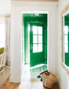 a green door in a white room with two mirrors and a purse on the floor