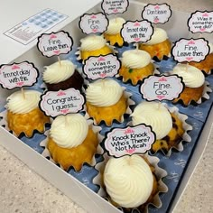 cupcakes with white frosting in a box on the counter top for sale