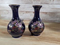 two blue vases sitting on top of a wooden table with flowers painted on them