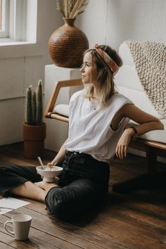 a woman sitting on the floor with her legs crossed and holding a cup in front of her