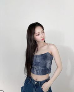 a woman with long hair standing in front of a white wall wearing blue jeans and a crop top