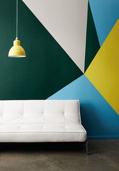 a white couch sitting in front of a green and blue wall with a yellow light hanging from it