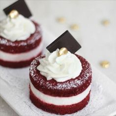 two red velvet desserts with white frosting and gold decorations on a white plate