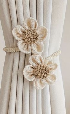 two flowers are attached to the back of a white curtain with beige pleated drapes