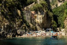 the beach is crowded with people and umbrellas in the shade, near some cliffs