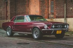 an old red car is parked on the side of the road in front of brick buildings