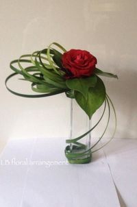 a red rose in a clear vase filled with water and greenery on a white surface